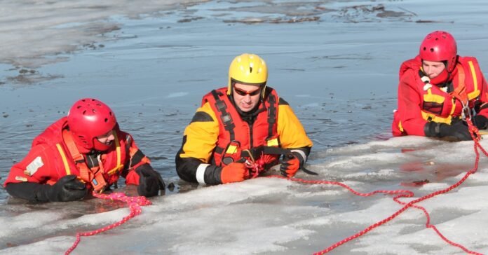 Three people wearing life jackets in freezing water surrounded by ice, demonstrating winter survival and self-preparedness.